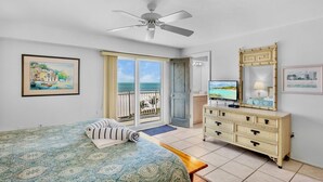 Een hotelkamer met een bed, een dressoir, een televisie en een balkon met uitzicht op zee.