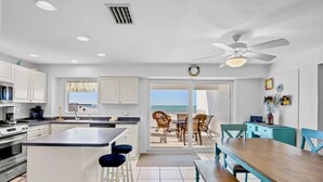 Een moderne keuken met witte kasten, een centraal eiland en een eetruimte met uitzicht op de oceaan.
