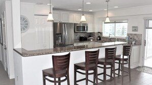 A modern kitchen with white cabinets, stainless steel appliances, and a large island with bar stools. - Experience Siesta Key Beach at Jamaica Royale 504 – Your Perfect Beach Escape! (Siesta Key)