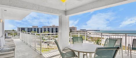 A balcony with a table and chairs, a ceiling fan, and a view of the beach and buildings.