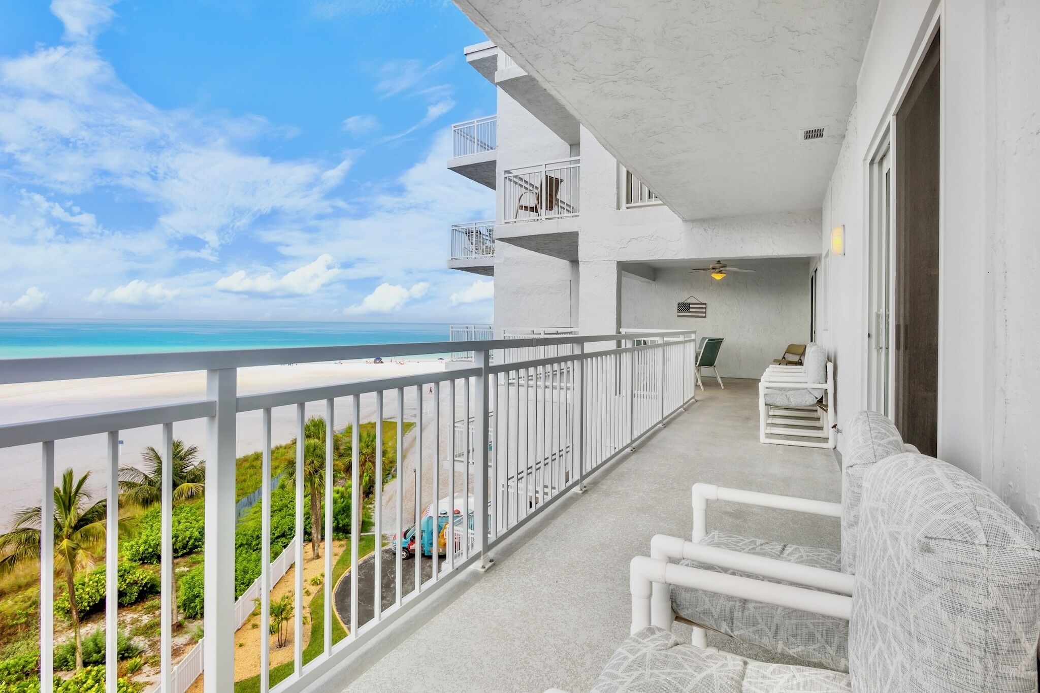 A balcony with a view of the ocean, a white railing, and a seating area with a sofa and chairs.