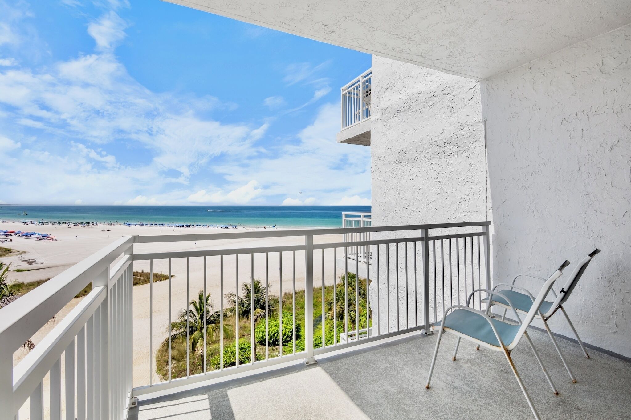 A balcony with a view of a beach and ocean. There are two chairs and a railing.
