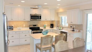 A modern kitchen with white cabinetry, a central island with chairs, a microwave, a stove, and a coffee maker. - Jamaica Royale 603 Nicely updated and Great views! (Siesta Key)