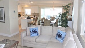 A modern living room with a beige sofa, two blue crab-patterned pillows, a glass coffee table, and a large potted plant. - Jamaica Royale 603 Nicely updated and Great views! (Siesta Key)