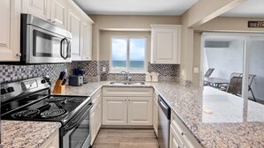 A kitchen with white cabinets, a stainless steel stove, a microwave, and a window with a view of the ocean. - Jamaica Royale 604 Beautfully updated and great views! (Siesta Key)
