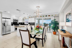 A modern kitchen with white cabinetry, a stainless steel refrigerator, and a dining area with a glass table and chairs.