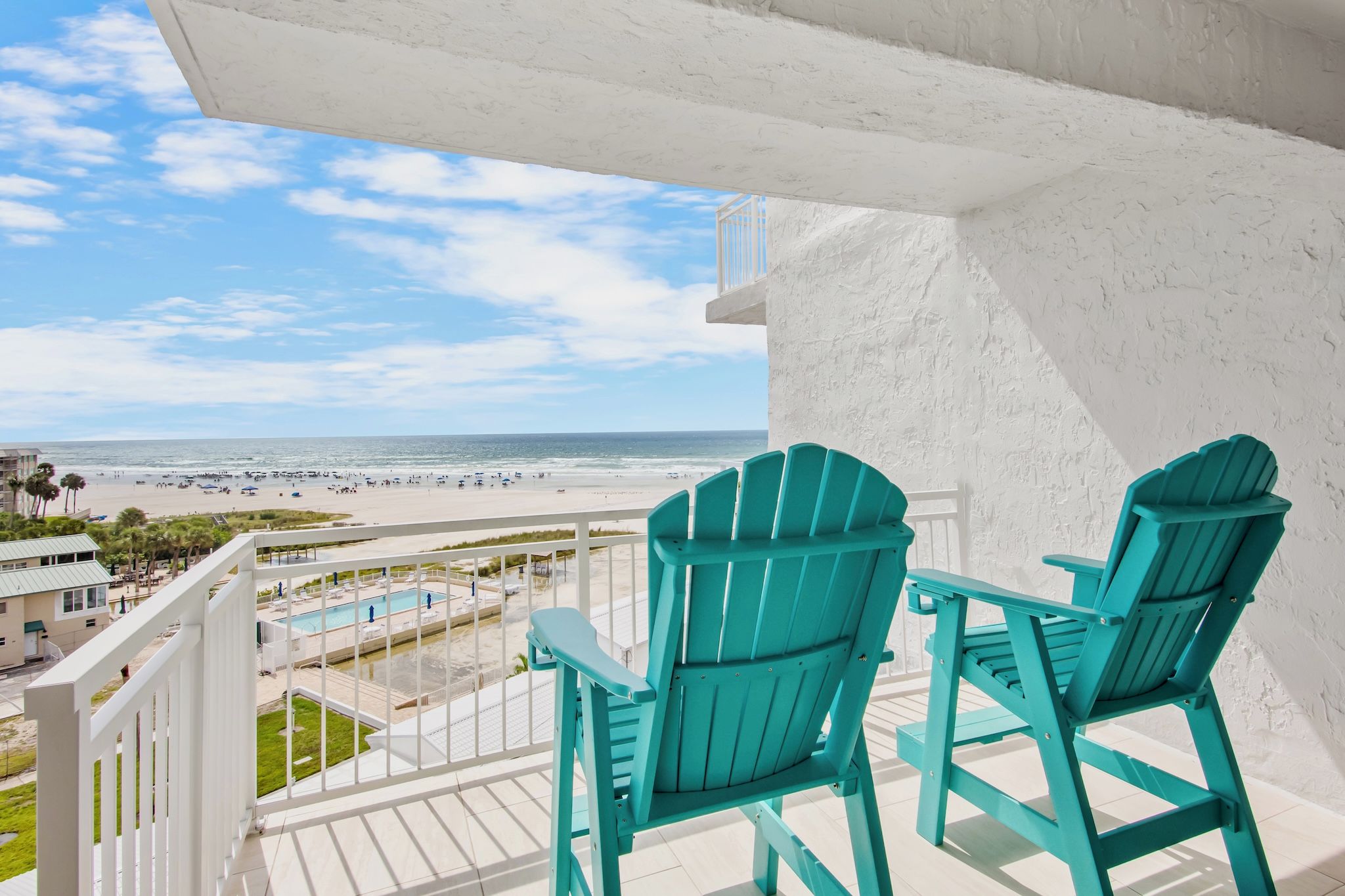 A balcony with two chairs overlooking a beach and a pool.