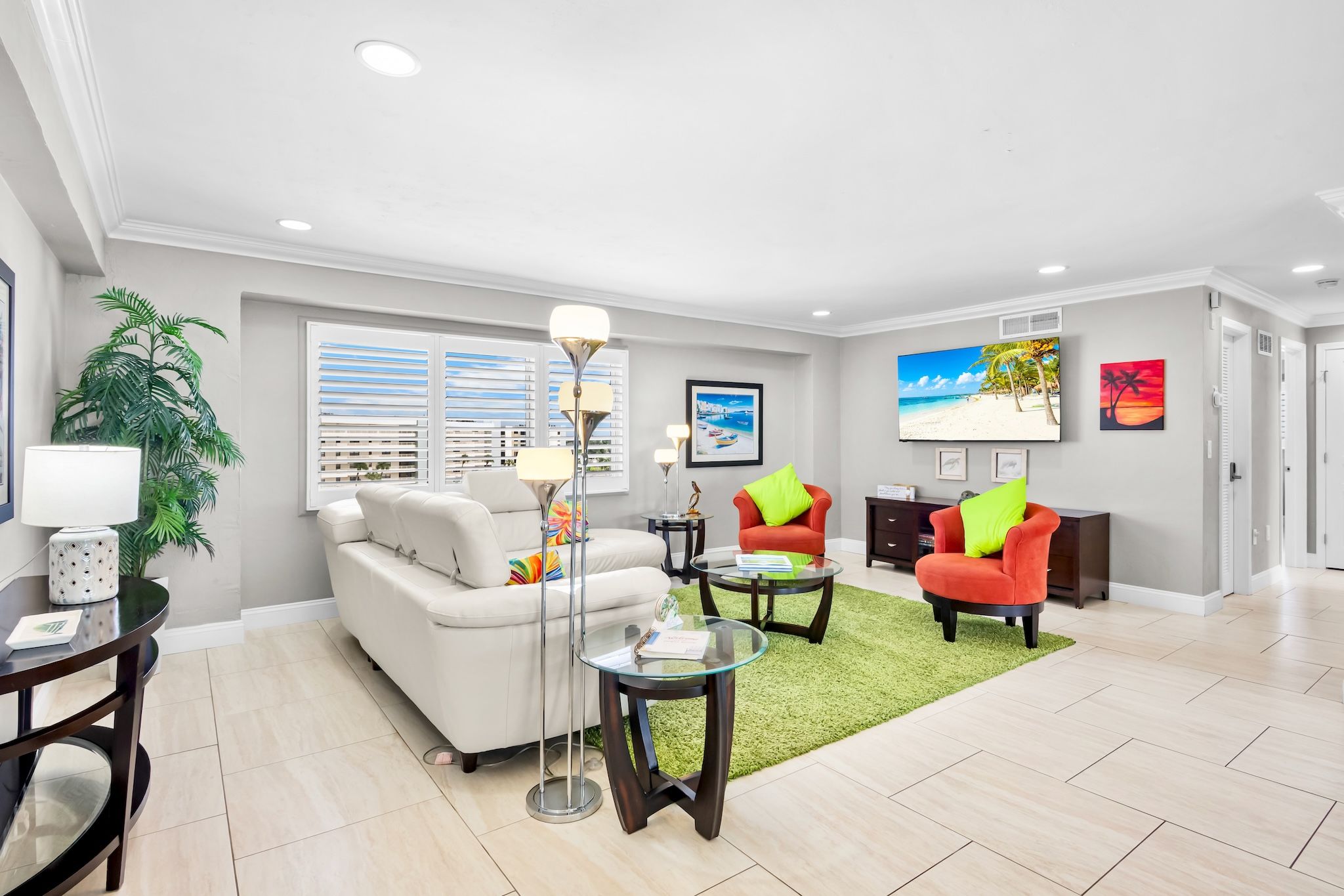 A modern living room with a white sofa, red chairs, a glass coffee table, and a green rug.