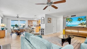 A spacious living area with a large TV, ceiling fans, and a view of the ocean.