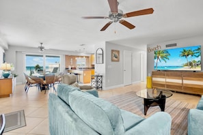 A spacious living area with a large TV, ceiling fans, and a view of the ocean.