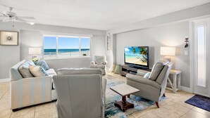 A living room with a large window, a television, and a ceiling fan. - Experience the Best of Siesta Key at Jamaica Royale 702 with Gulf Views! (Siesta Key)
