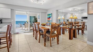 A dining area with a large table and chairs, a view of the ocean through a glass door, and a kitchen visible through the glass. - Experience the Best of Siesta Key at Jamaica Royale 702 with Gulf Views! (Siesta Key)