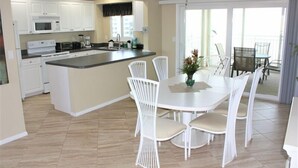Een moderne keuken met witte kastjes, een centraal eiland en een eethoek met witte stoelen.