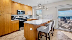 A modern kitchen with wooden cabinets, stainless steel appliances, and a large island with bar stools. - Family Beach Getaway at Jamaica Royale 705 in Siesta Key! (Siesta Key)