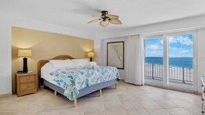 A hotel room with a bed, bedside lamps, a ceiling fan, a large window with a view of the beach, and a framed picture on the wall. - Couples Beachfront Getaway at Jamaica Royale 801 in Siesta Key! (Siesta Key)