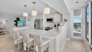 Cozinha moderna com ilha central, armários brancos e iluminação pendente.