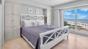 Quarto com cama, guarda-roupa branco e vista para a praia.