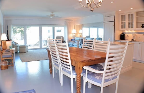 A spacious dining area with a wooden table and white chairs, a kitchen with white cabinets, and a balcony with a view.