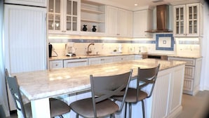Una cocina con armarios blancos, encimera de mármol y una isla integrada con taburetes de bar.