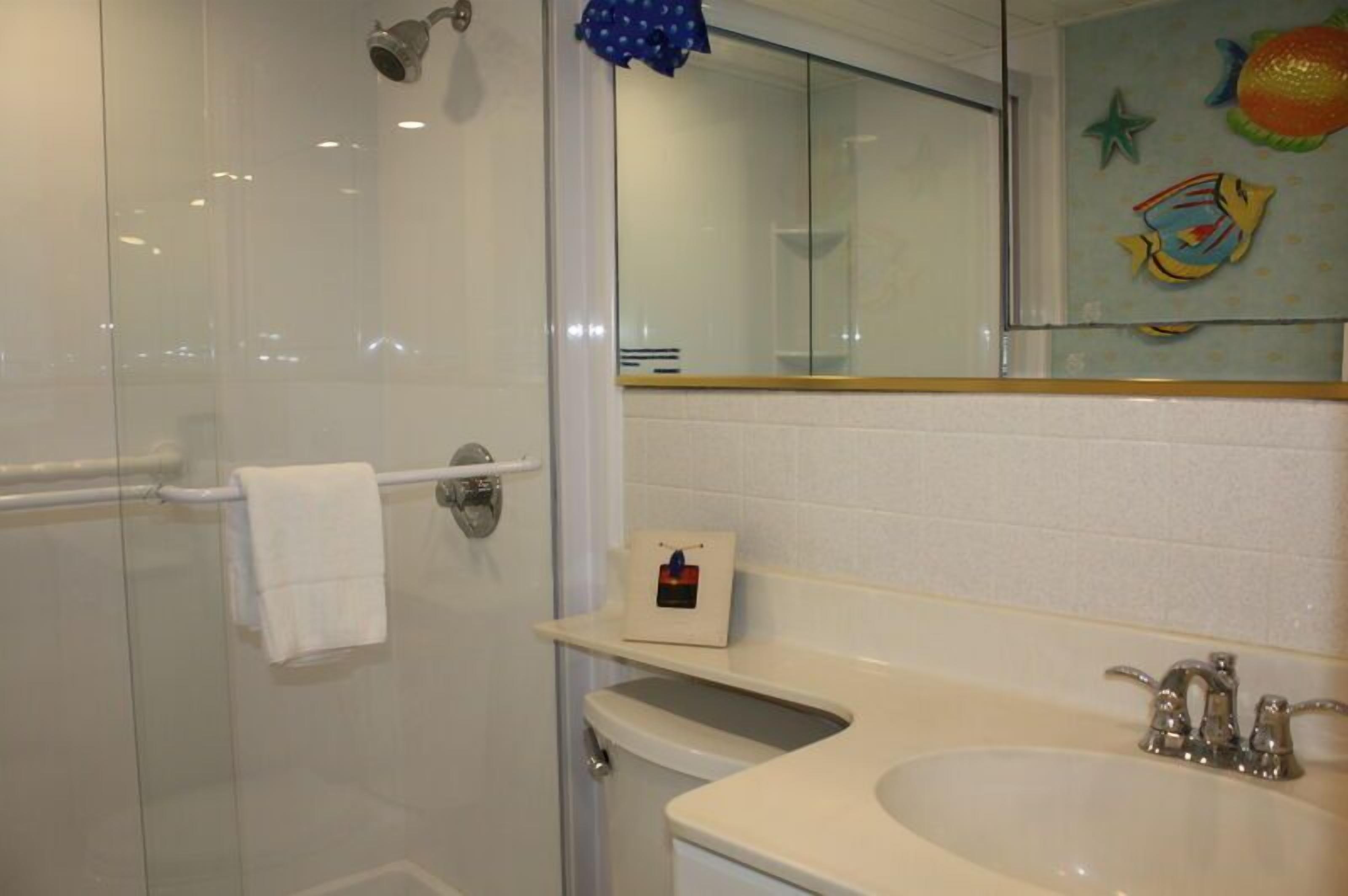 Un baño con cabina de ducha de vidrio, un lavabo blanco y un espejo con calcomanías decorativas de peces.