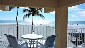 Un balcon avec vue sur la plage, deux chaises blanches et une table ronde.