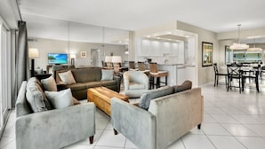 A modern living room with a sofa set, a coffee table, and a TV. There is a dining area with a table and chairs, and a kitchen with cabinets and a countertop. - Jamaica Royale T43 Nice updates and Great views! (Siesta Key)