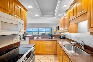A modern kitchen with wooden cabinets, a stainless steel sink, and a view of the beach. - Beachfront Bliss: Jamaica Royale T51 - Private Balcony with Beach Views! (Siesta Key)