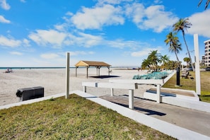 A beachside view with a wooden deck, lounge chairs, and a covered seating area.