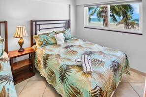 A bedroom with a bed, a nightstand, a lamp, and a window with a beach view. - Beachfront Bliss: Jamaica Royale T51 - Private Balcony with Beach Views! (Siesta Key)