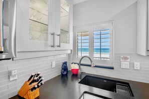 A modern kitchen with a black countertop, stainless steel appliances, and a view of the ocean through a window.