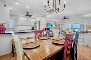 A modern kitchen with white cabinets, a dining table with woven placemats, and a chandelier.
