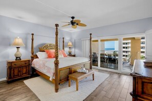 Une chambre dotée d’un lit à baldaquin, d’un ventilateur de plafond, offrant une vue sur la plage grâce à ses portes-fenêtres coulissantes, et d’un balcon aménagé avec du mobilier d’extérieur.