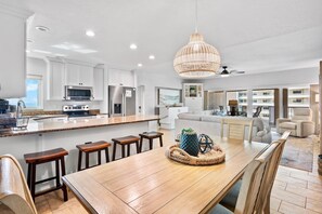 Une cuisine moderne avec des meubles blancs, un grand îlot central doté de tabourets et un coin repas avec une table et des chaises en bois.