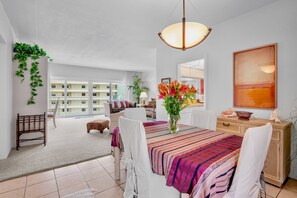 Een ruime woonkamer met een eettafel, stoelen, een bank, een lamp en uitzicht op een gebouw op de achtergrond.