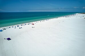 A wide sandy beach with clear turquoise water and a few umbrellas.