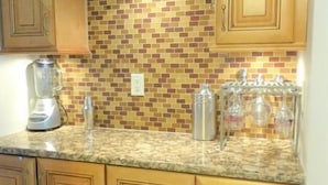 Eine Küche mit Holdekor-Schränken, einer gefliesten Spritzschutzwand, einer Arbeitsplatte aus Granit, einem Mixer und einem Glasbehälter.