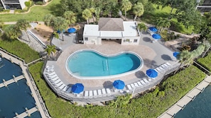 An aerial view of a resort with a central swimming pool, lounge chairs, and umbrellas.