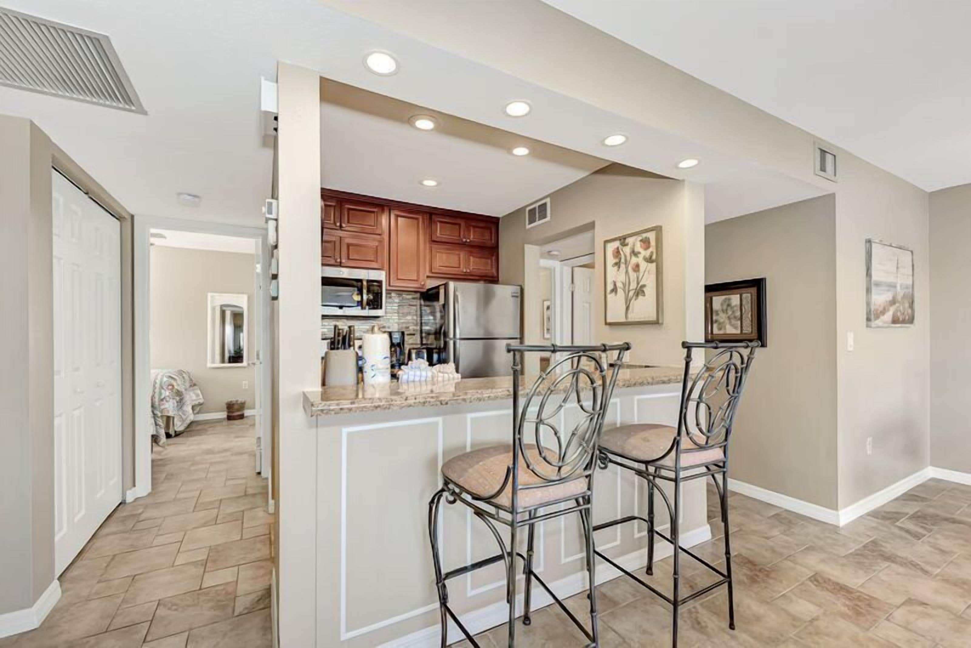 A kitchen with a central island, two bar stools, wooden cabinets, and a refrigerator.