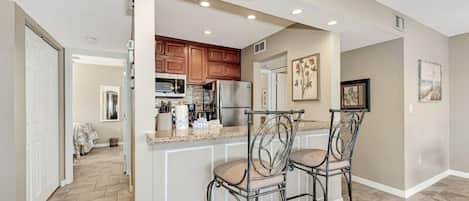A kitchen with a central island, two bar stools, wooden cabinets, and a refrigerator.