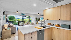 A modern kitchen with wooden cabinets, a built-in dishwasher, and a large island with a cutting board. - Midnight Cove II 212F - Breathtaking Bay View - Beach Decor! (Siesta Key)