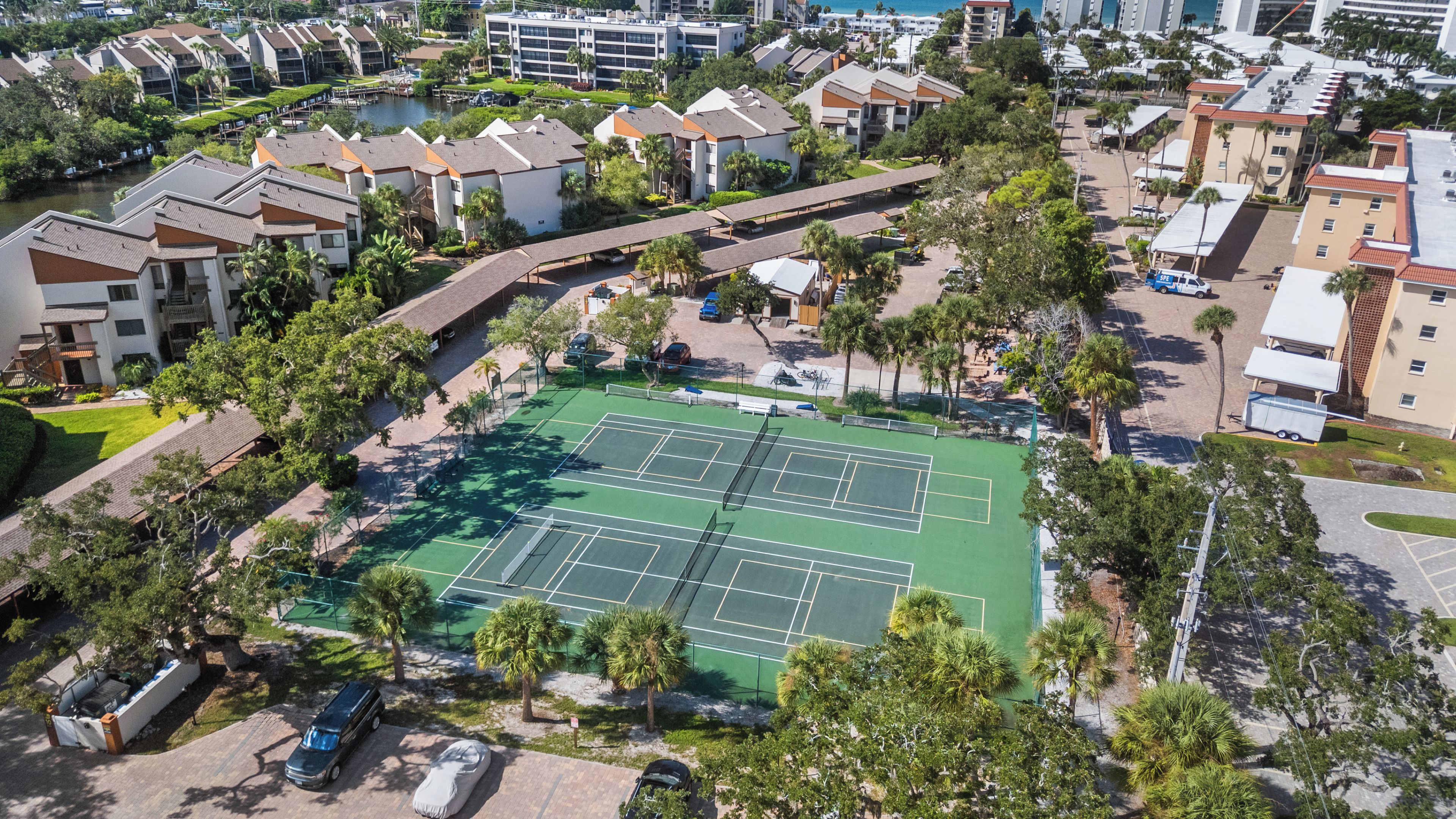 Vue aérienne d’un quartier résidentiel avec un court de tennis entouré d’immeubles et de palmiers.