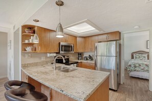 A modern kitchen with a central island, stainless steel appliances, wooden cabinets, and a skylight.