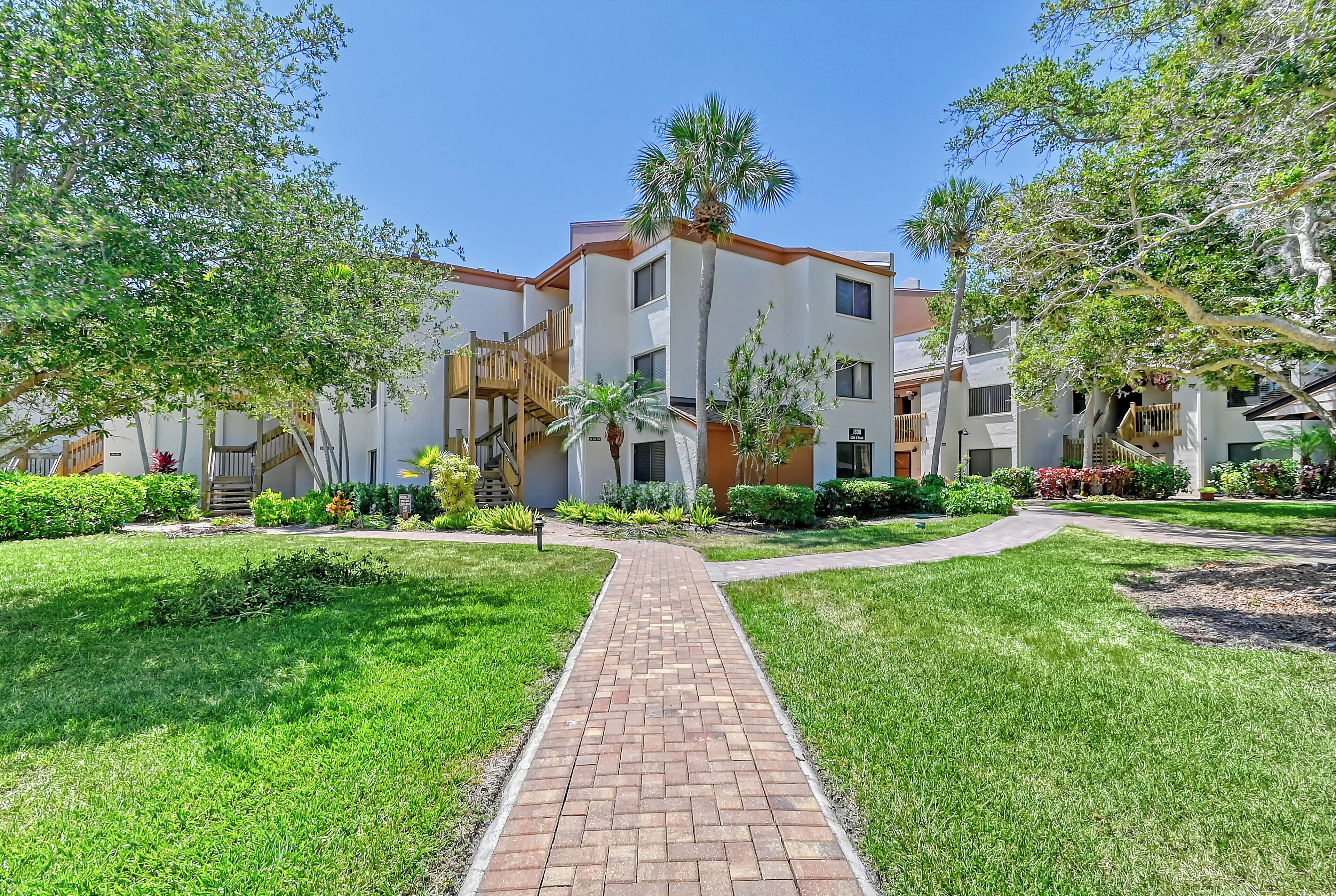 A residential building with a brick pathway, green lawns, and palm trees.