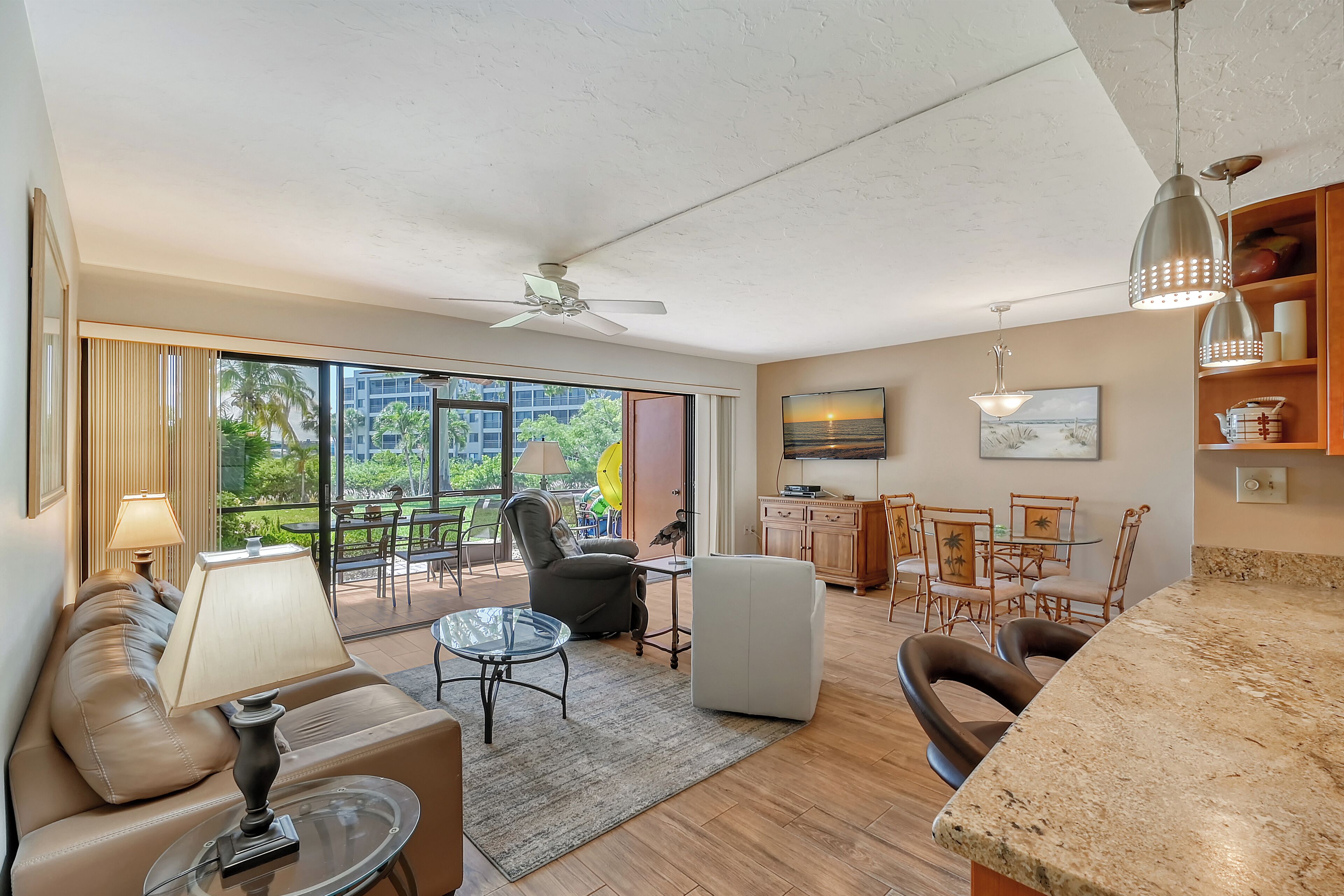 A spacious living area with a sofa, a glass coffee table, a dining table with chairs, and a view of the outdoors through large windows.