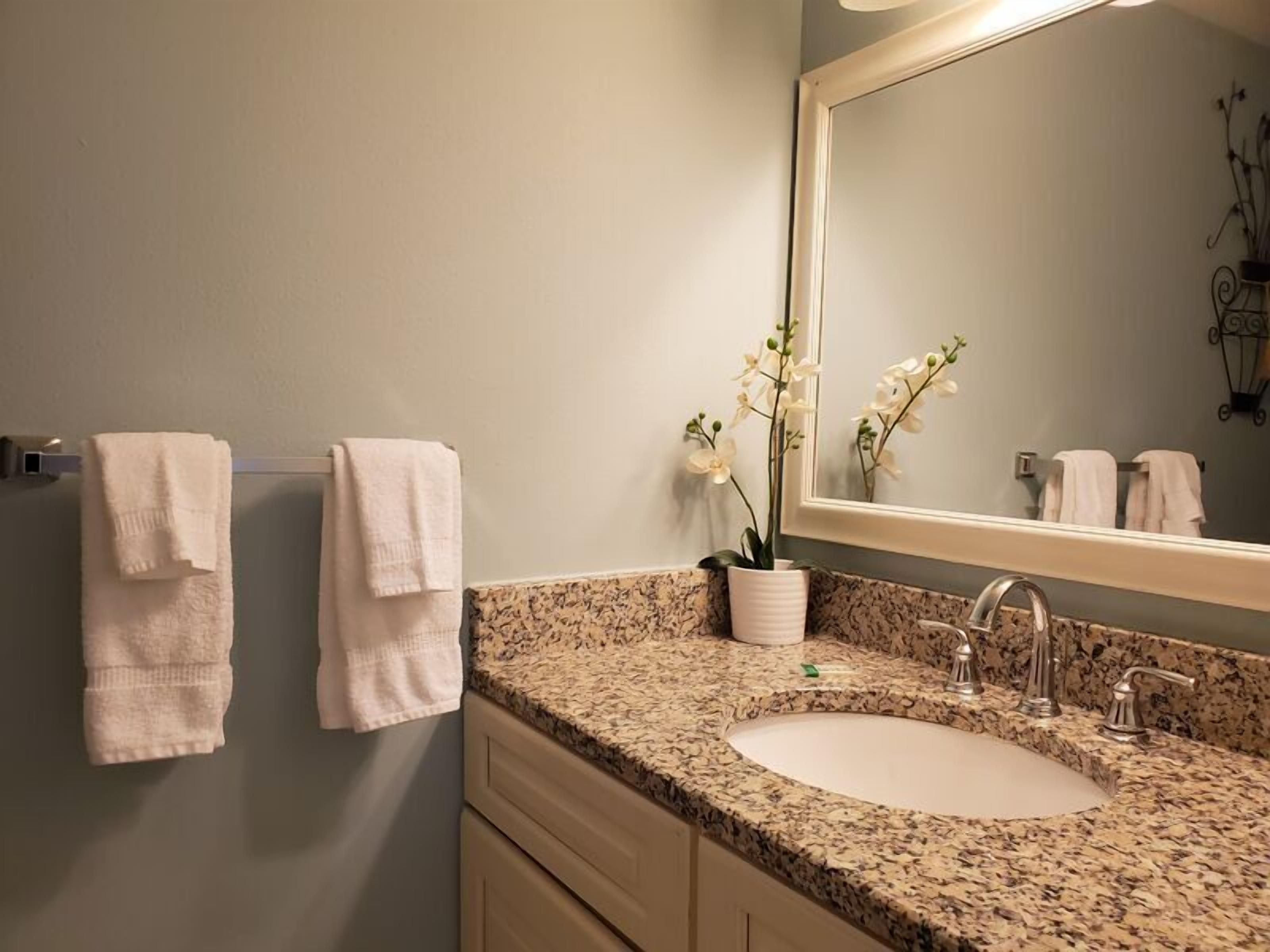 A bathroom with a granite countertop, a white sink, and a mirror. There are two towels hanging on the wall.