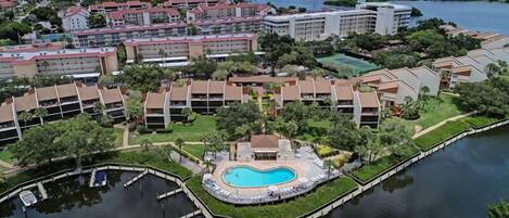 A resort with multiple buildings, a central swimming pool, and a body of water.