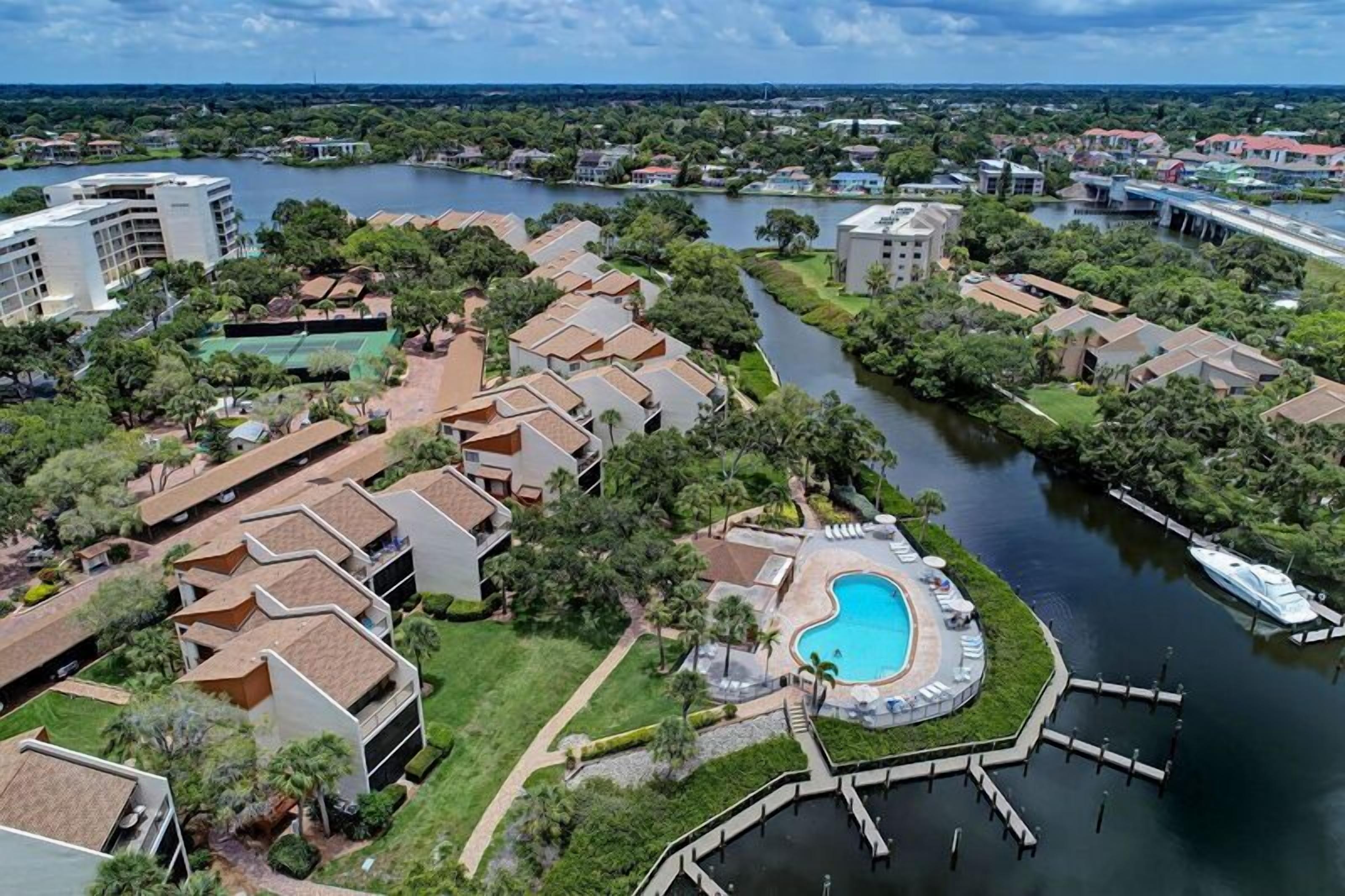 An aerial view of a resort with a swimming pool, docked boats, and a river.