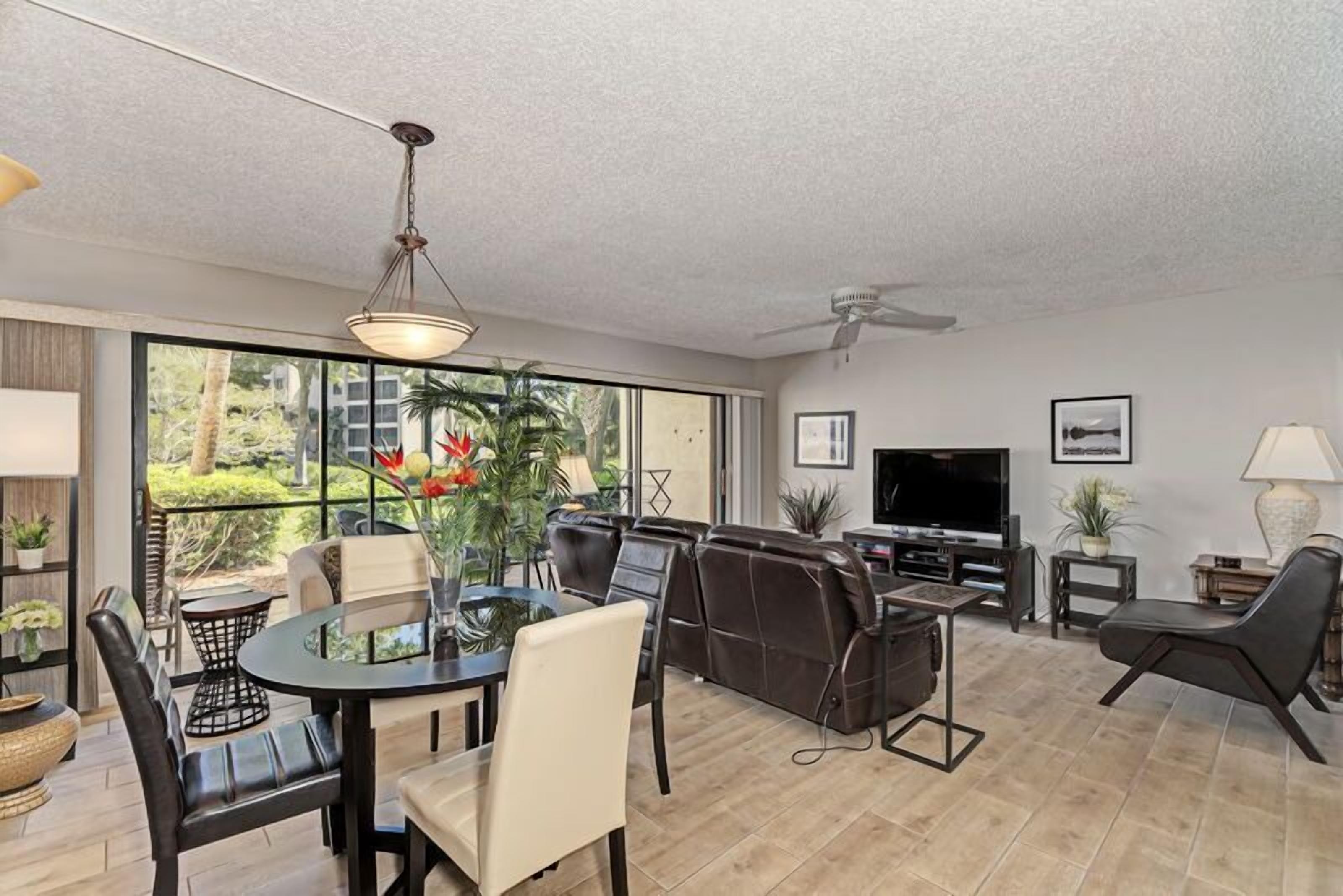 A modern living room with a dining area, a large TV, and a ceiling fan.