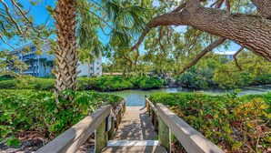 A wooden boardwalk leading to a river, surrounded by lush greenery and trees. - Midnight Cove II 313F: Siesta Key Condo with Beach, Pool, Pickleball Access (Siesta Key)