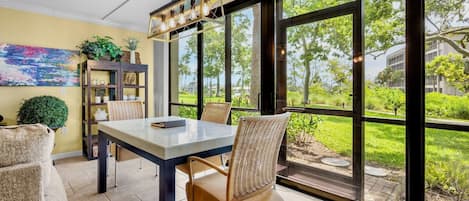 A dining area with a table and chairs, large windows, and a view of greenery outside.